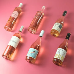 Six bottles of rosé wine arranged on a pink background