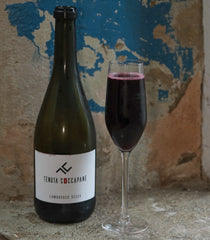Bottle and glass of red wine with Tenuta Coccapane label against a textured wall.