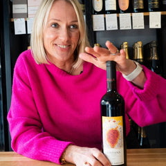 Kate Goodman wears a vibrant pink jumper while smiling in a wine shop and holding a bottle of Marco Abella Loidana Priorat